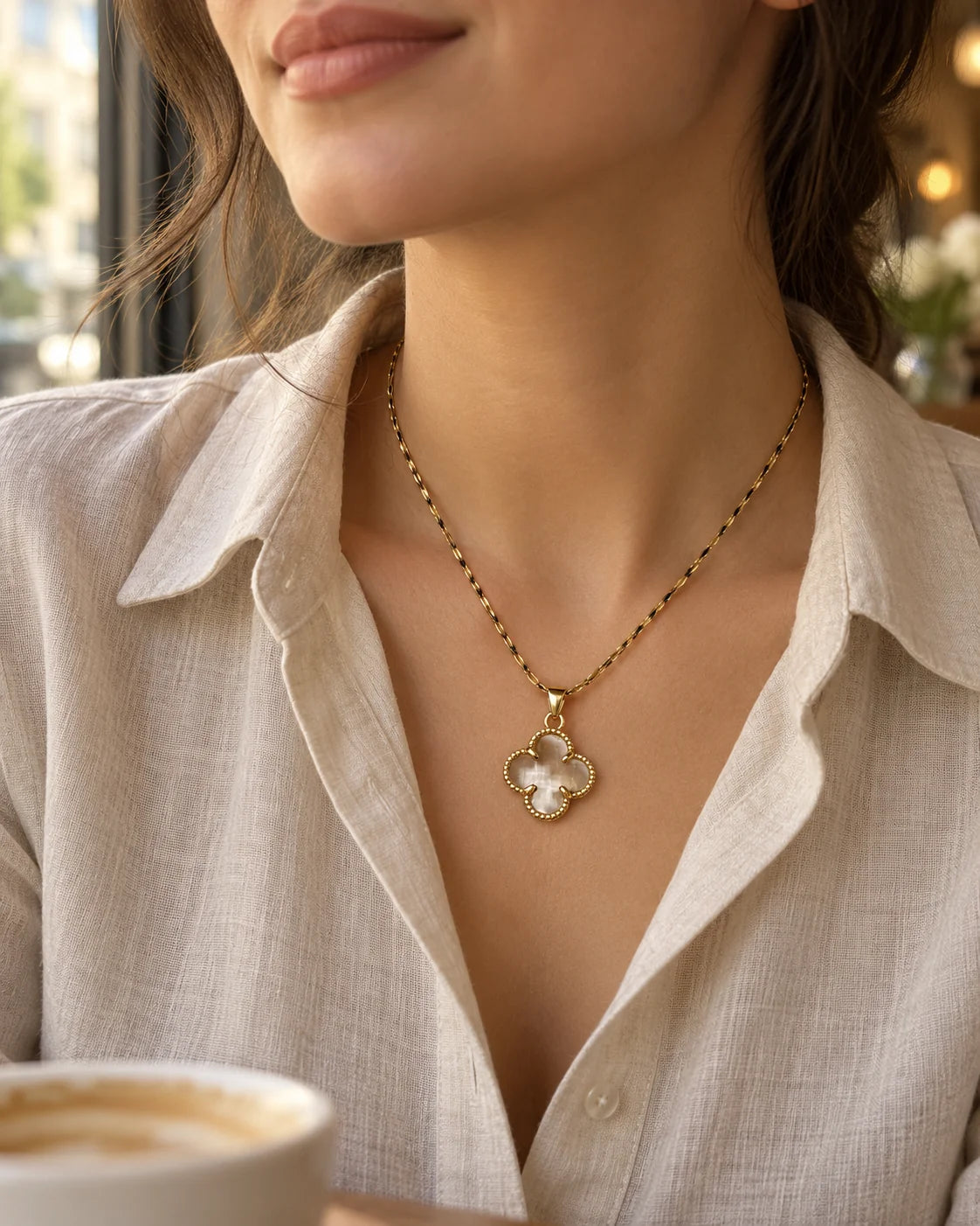 Model in a linen shirt wearing the Fortuna clear clover necklace by a café window
