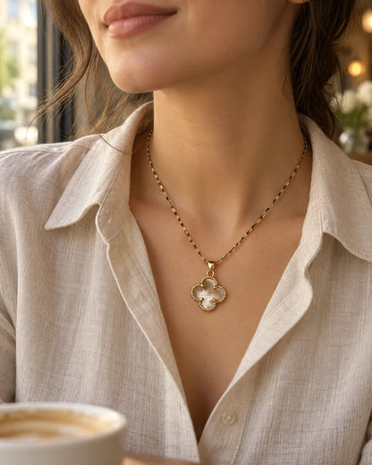 Model in a linen shirt wearing the Fortuna clear clover necklace by a café window