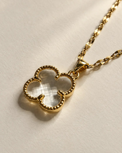 Fortuna clear clover pendant on a fine gold-tone chain resting on cream