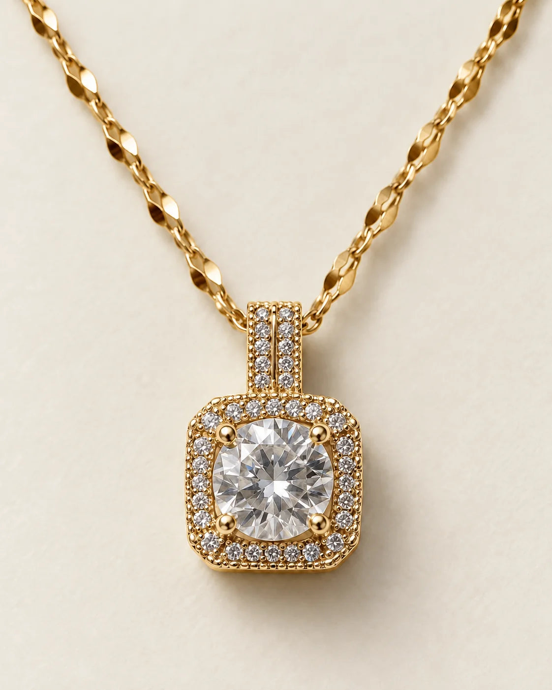 Celeste gold cushion halo pendant with a round clear centre stone on a cream background