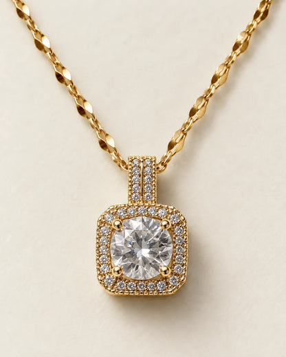 Celeste gold cushion halo pendant with a round clear centre stone on a cream background