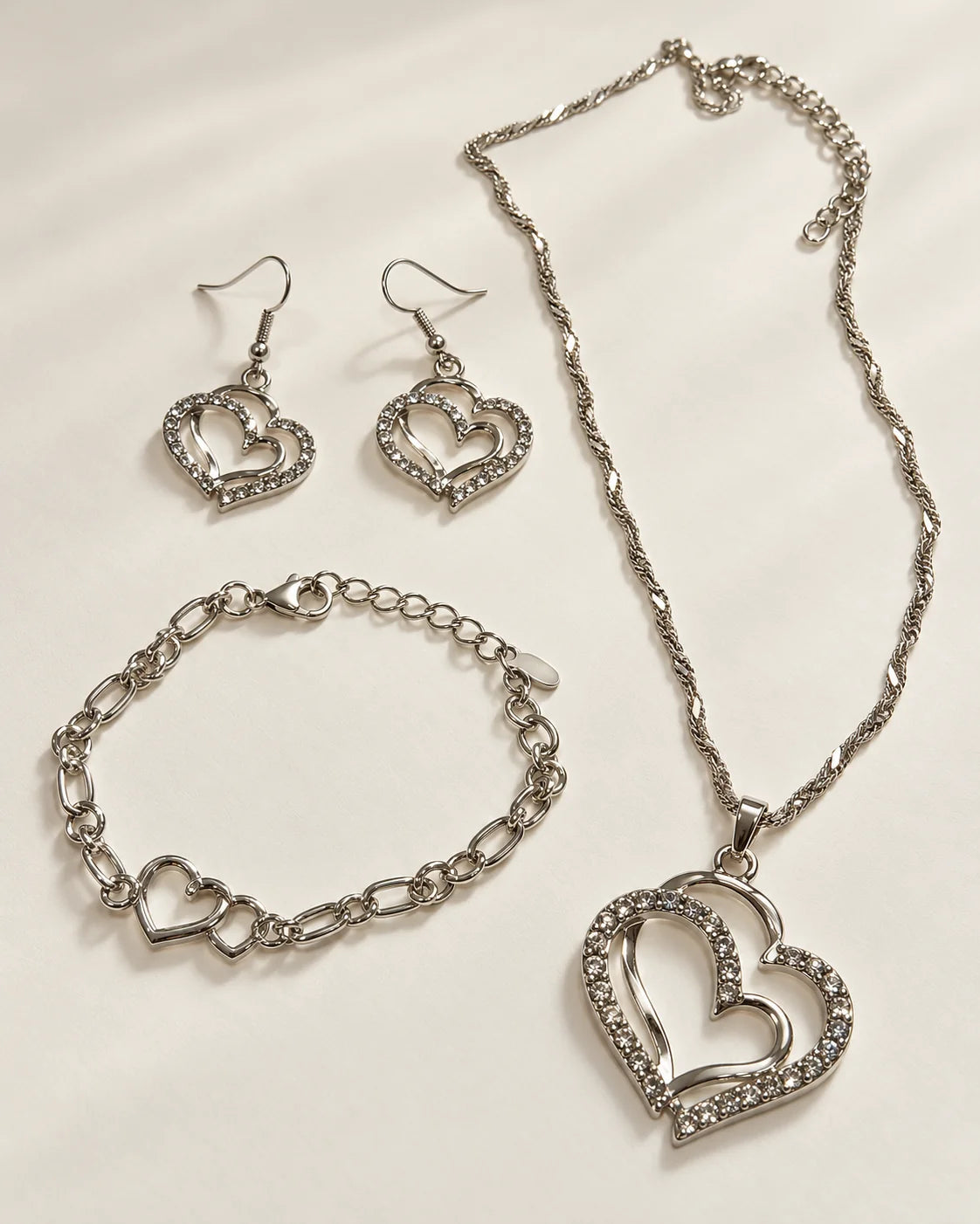 Everlinked silver double heart necklace, earrings and bracelet set laid flat on cream