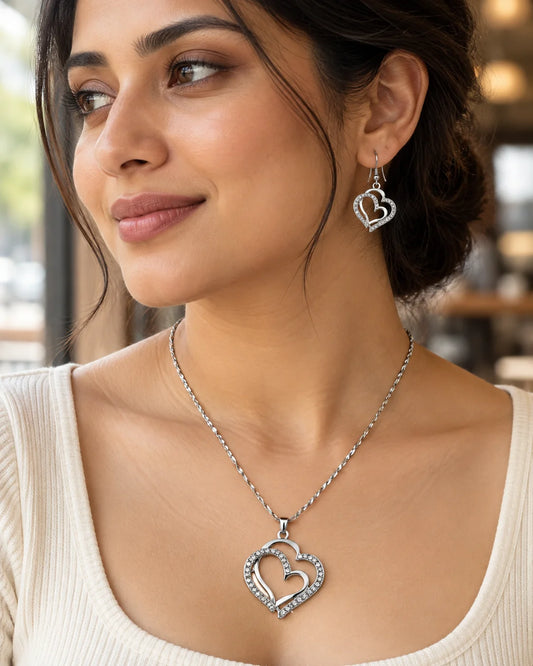 Woman by a window wearing the silver double heart pendant necklace and hook earrings