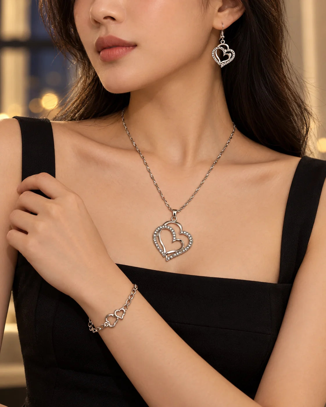 Woman in a black dress wearing the silver double heart necklace, earrings and bracelet