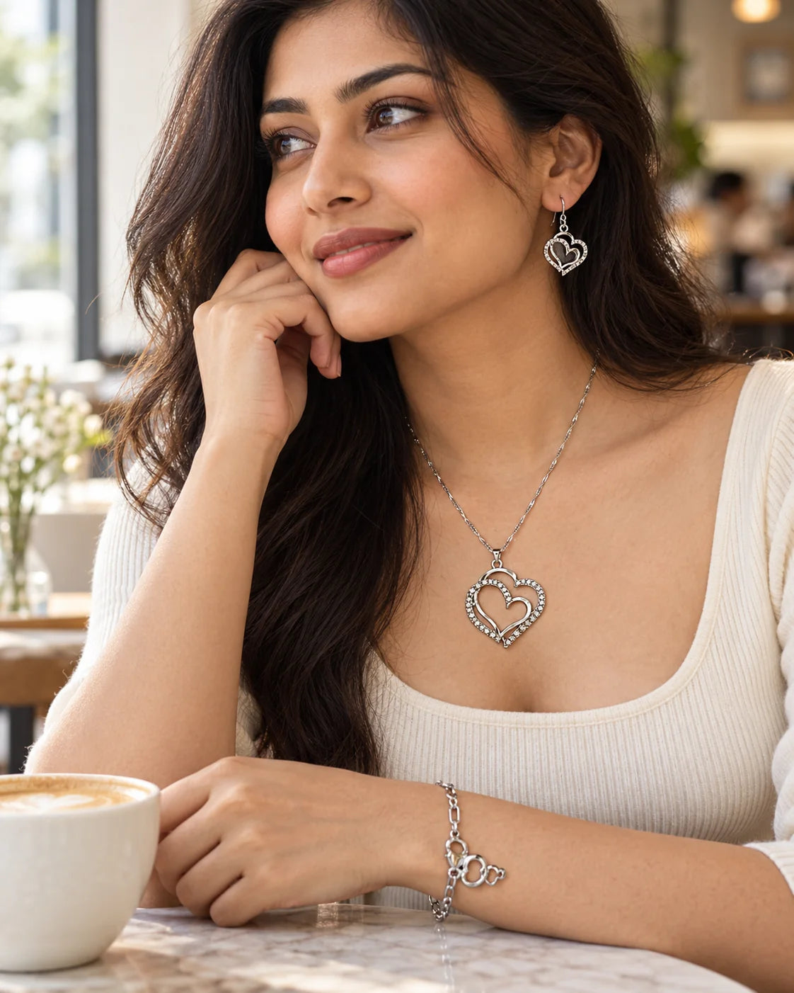 Woman in a café wearing the Everlinked silver double heart necklace, earrings and bracelet