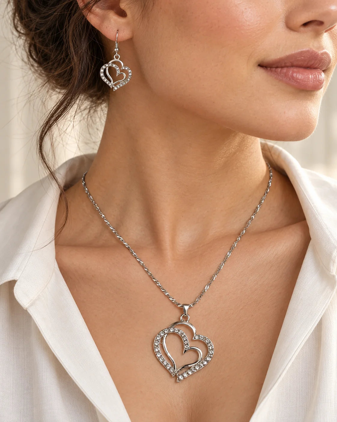 Woman in a white shirt wearing the silver intertwined heart necklace and earrings