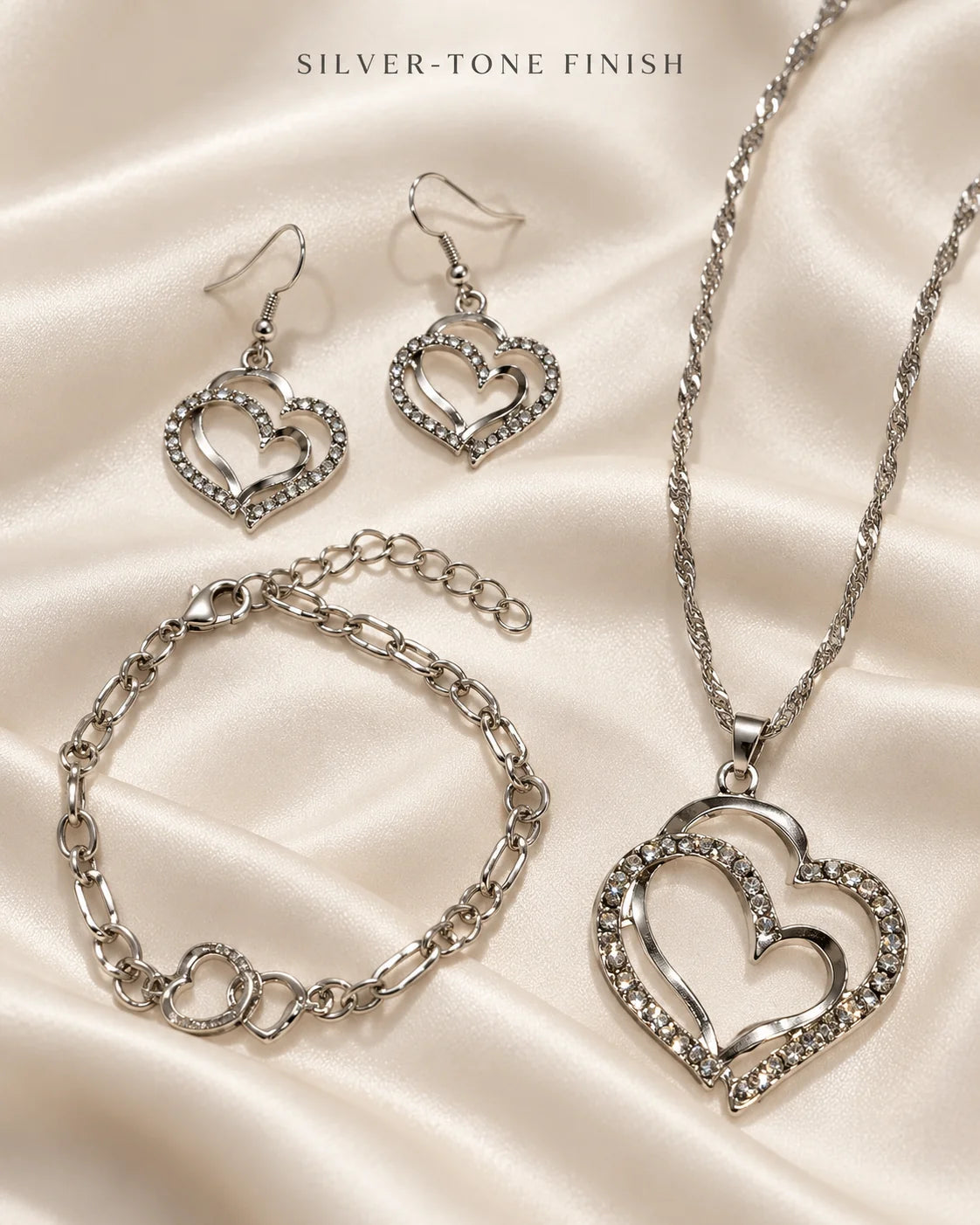 Silver-tone double heart necklace, earrings and bracelet on ivory satin