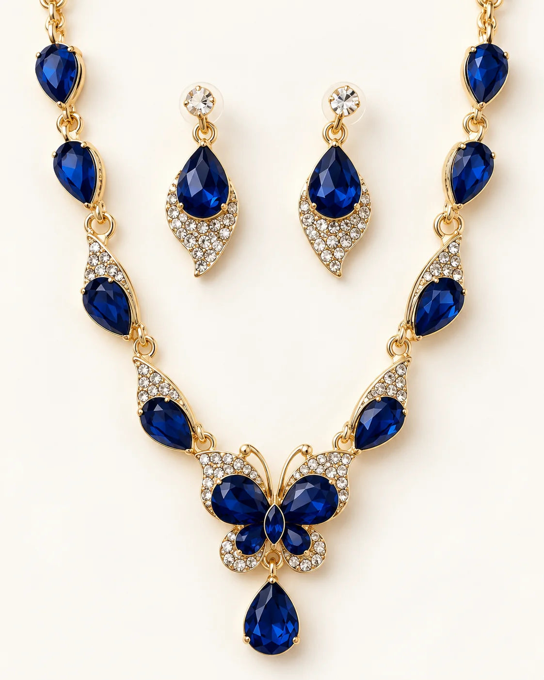 Papillon navy blue crystal butterfly necklace and earring set in gold tone laid flat on cream