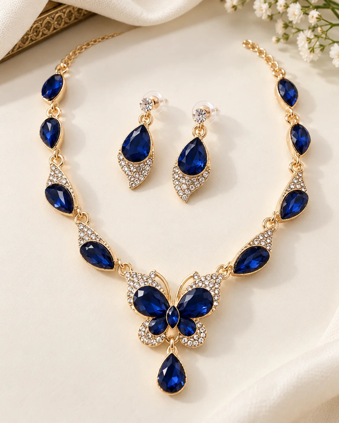 Navy blue butterfly necklace and teardrop earrings in gold tone styled with white flowers