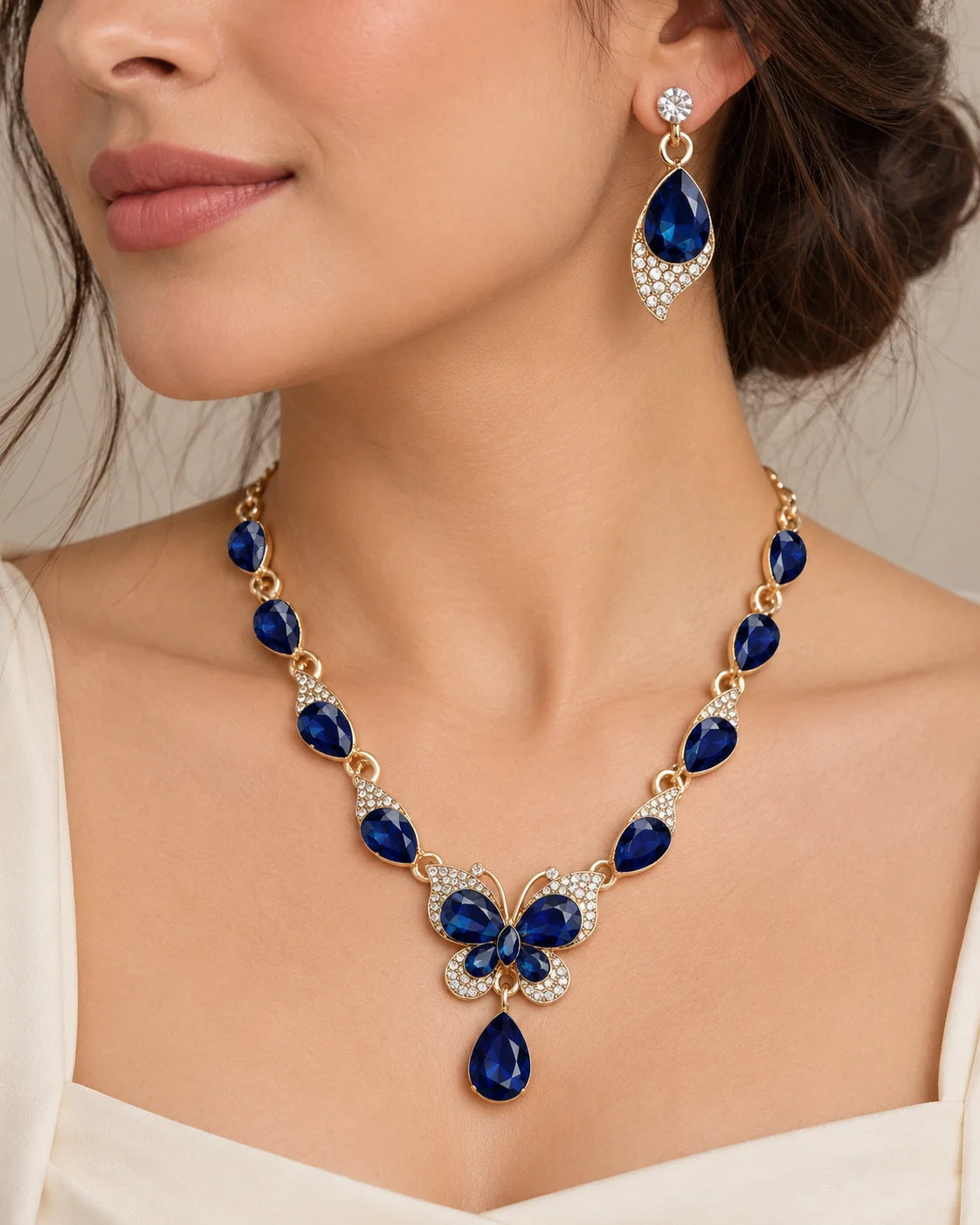 Woman wearing the navy blue butterfly necklace and drop earrings with an ivory top