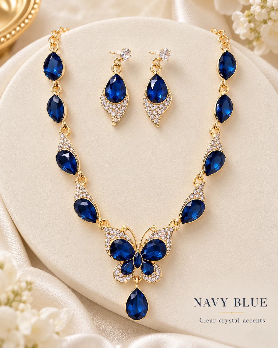 Navy blue butterfly jewellery set with clear crystal accents on a cream plinth