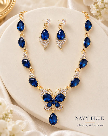 Navy blue butterfly jewellery set with clear crystal accents on a cream plinth