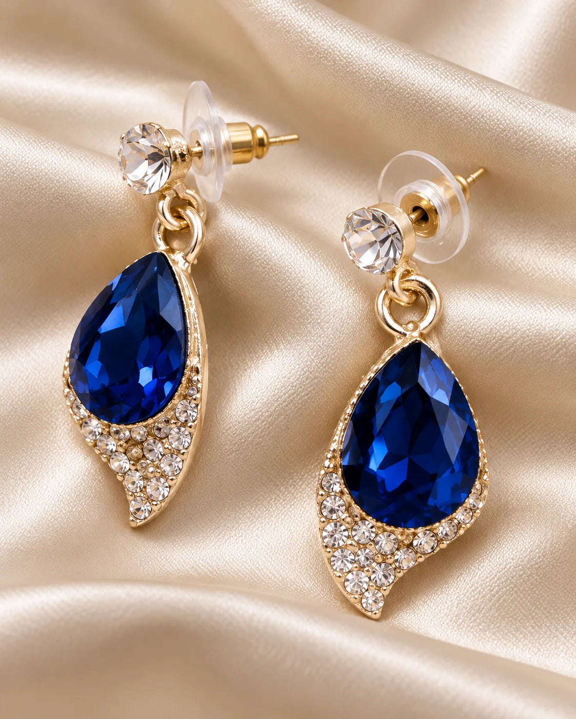 Close-up of navy blue teardrop earrings with rhinestone leaf frame on cream satin