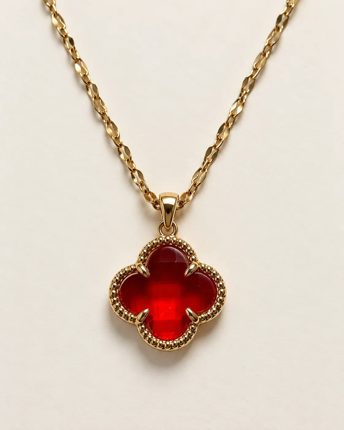 Fortuna cherry red clover pendant with a beaded gold-tone border on a cream background