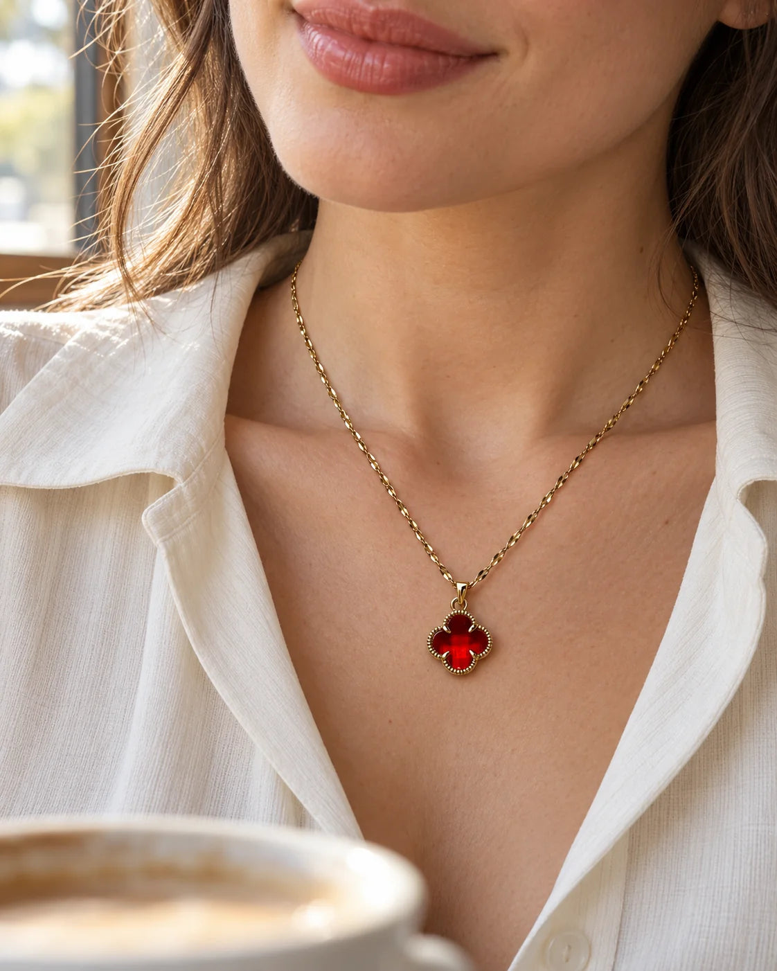 Model in a white shirt wearing the Fortuna cherry red clover necklace in café light