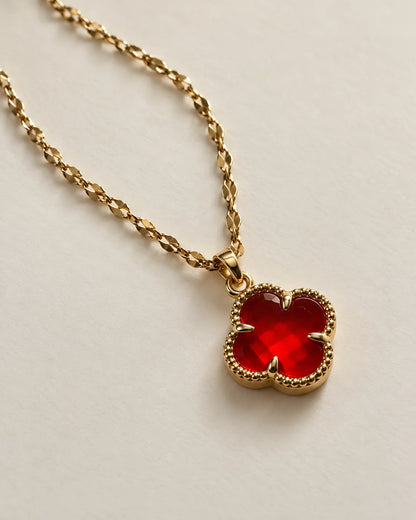 Fortuna cherry red clover pendant on a gold-tone chain laid on ivory