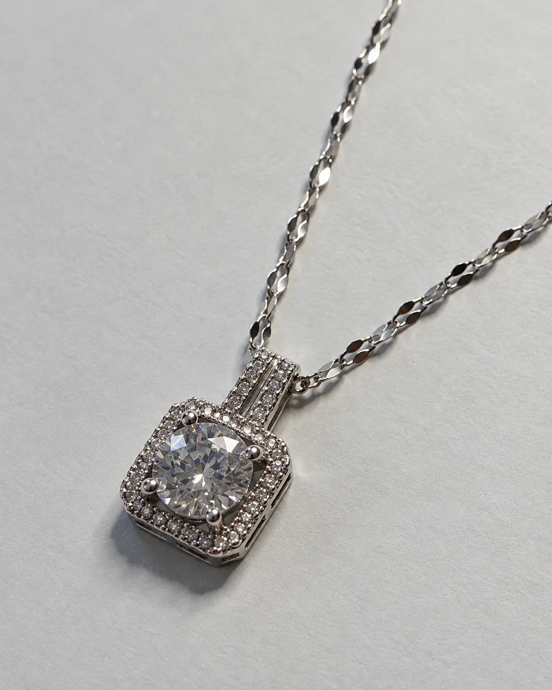 Celeste silver cushion halo pendant on a faceted link chain against soft grey