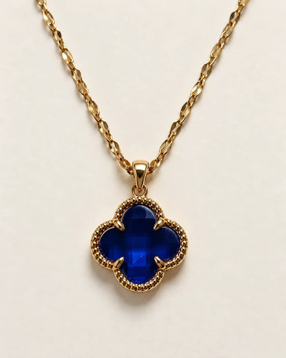 Fortuna sapphire blue clover pendant with a beaded gold-tone border on a cream background