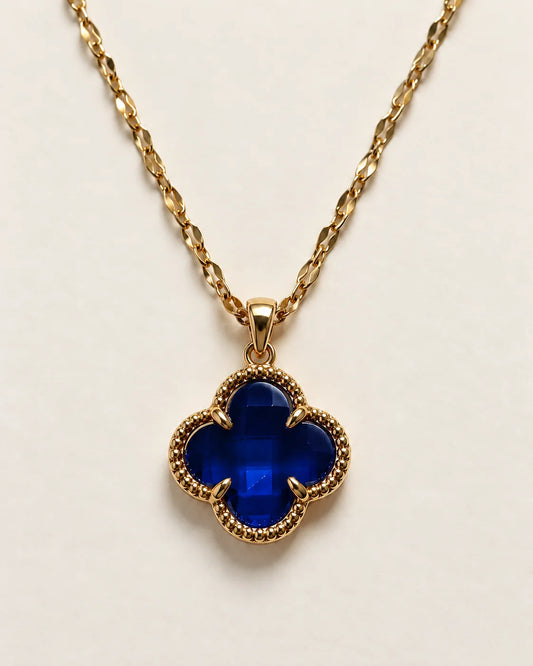 Fortuna sapphire blue clover pendant with a beaded gold-tone border on a cream background
