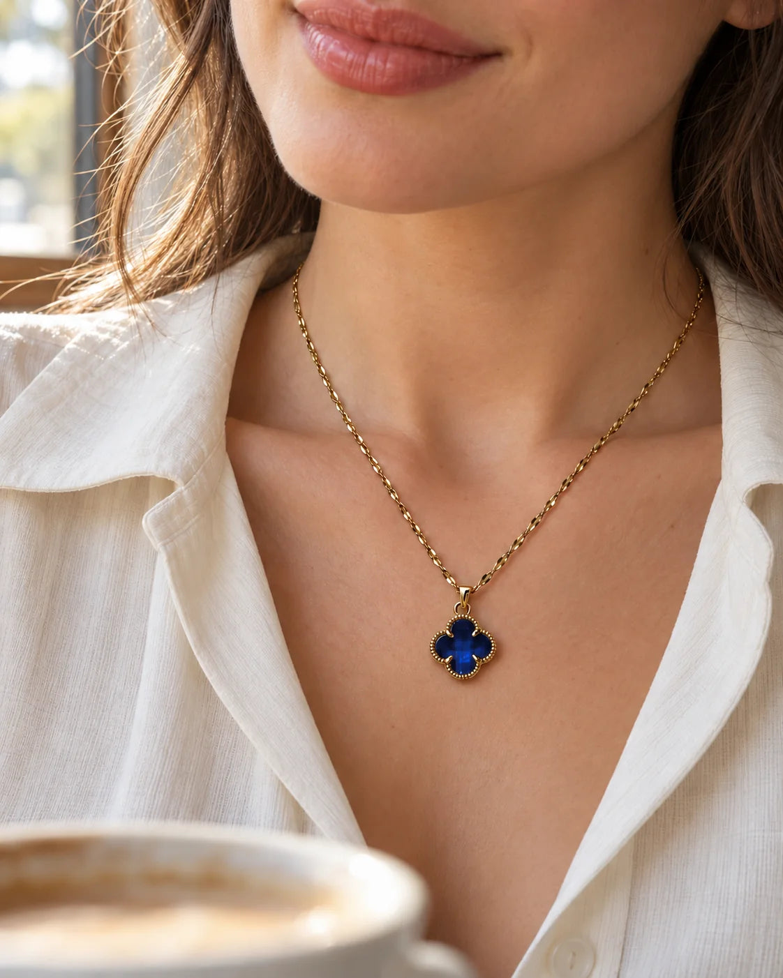 Model in a white shirt wearing the Fortuna sapphire blue clover necklace in café light