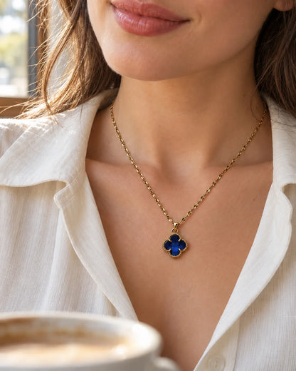 Model in a white shirt wearing the Fortuna sapphire blue clover necklace in café light