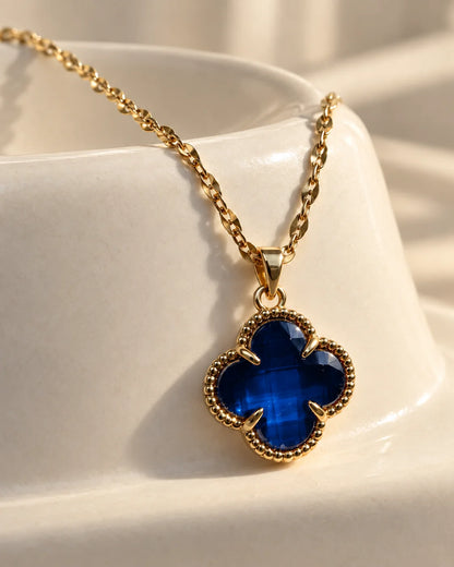 Fortuna sapphire blue clover pendant resting on an ivory ceramic dish