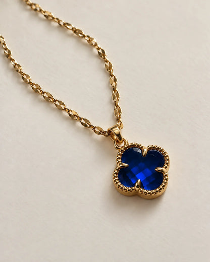 Fortuna sapphire blue clover pendant on a gold-tone chain laid on ivory