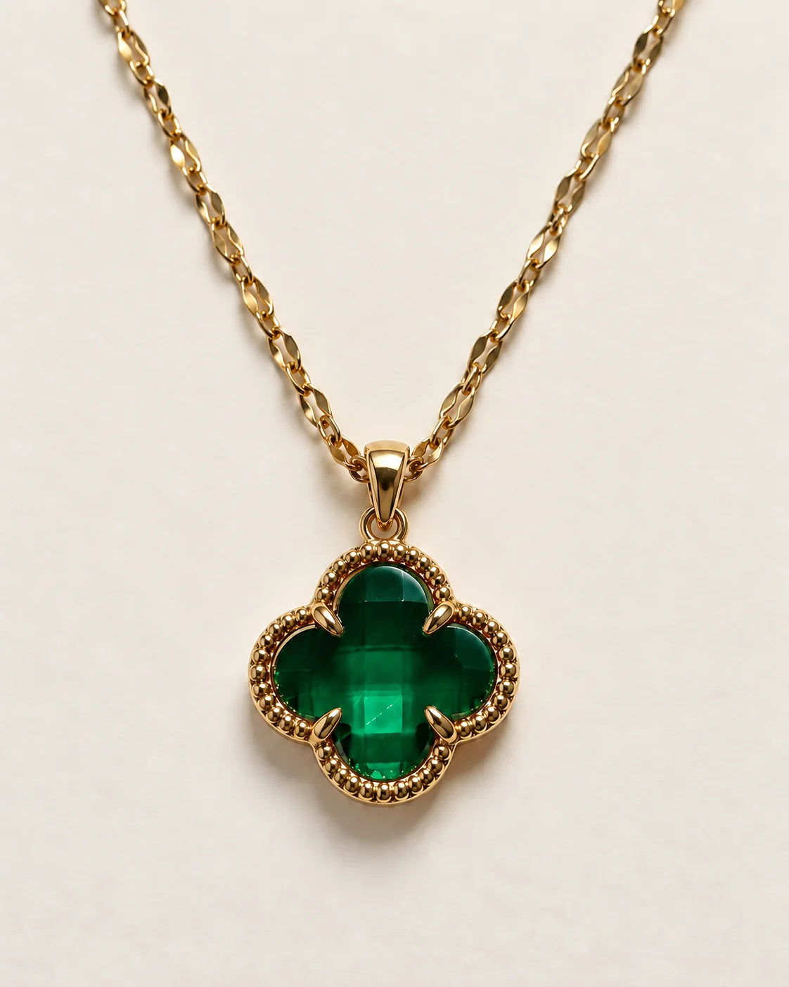Fortuna emerald green clover pendant with a beaded gold-tone border on a cream background
