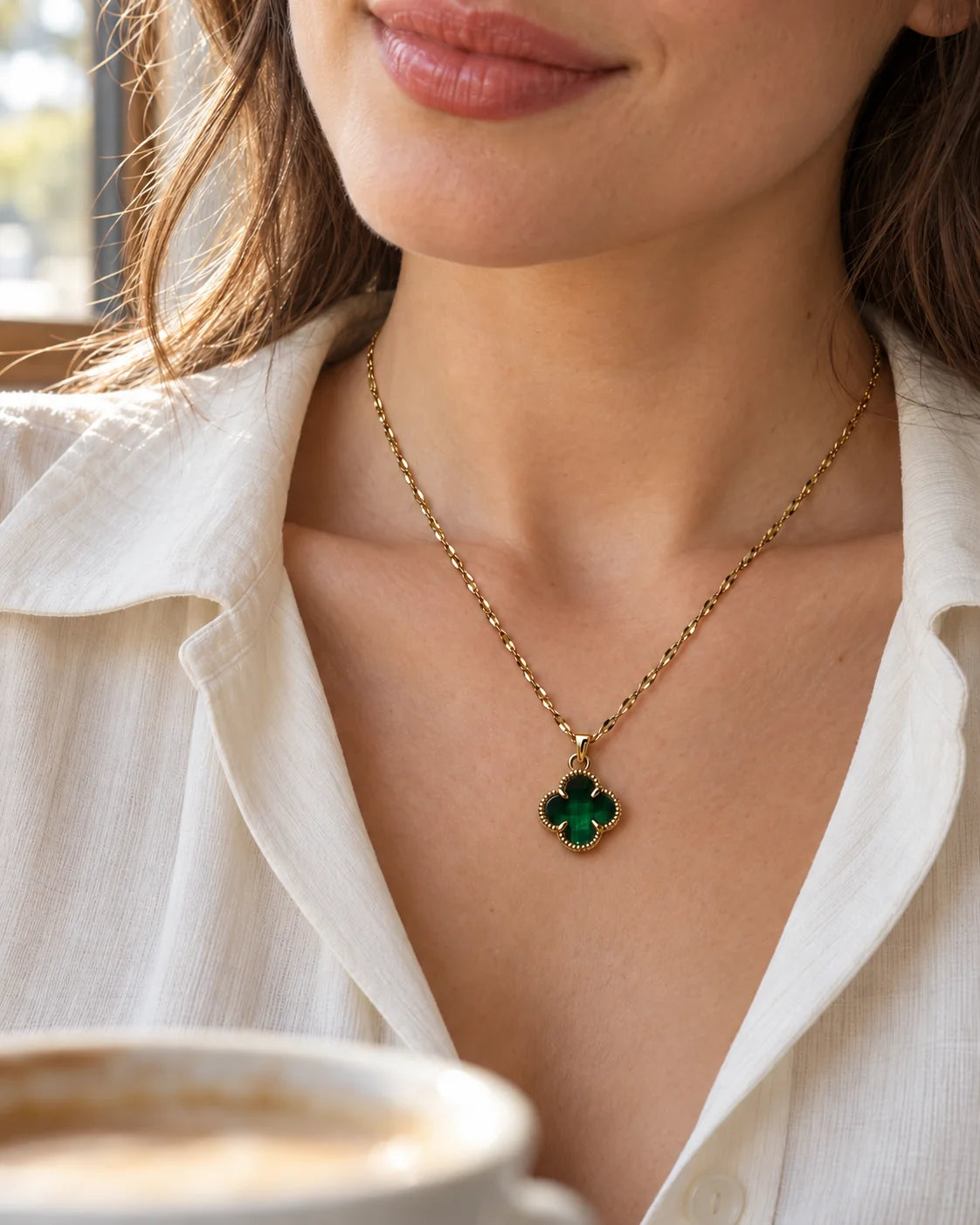 Model in a white shirt wearing the Fortuna emerald green clover necklace in café light