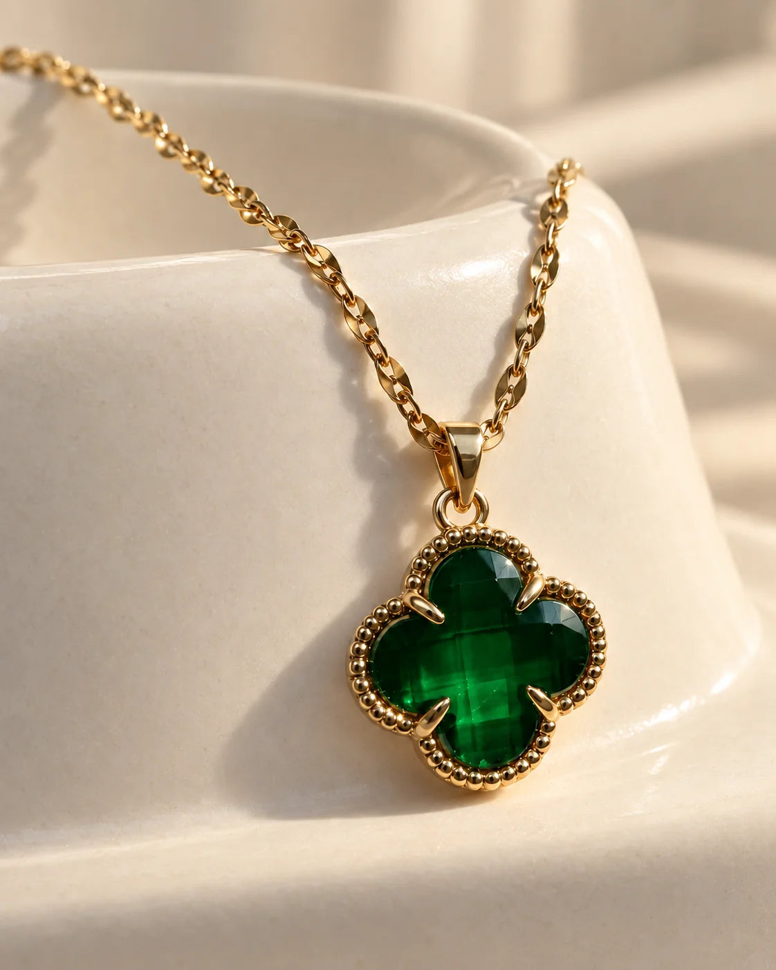 Fortuna emerald green clover pendant resting on an ivory ceramic dish