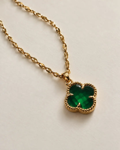 Fortuna emerald green clover pendant on a gold-tone chain laid on ivory