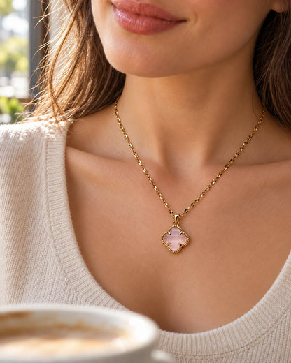 Model in a cream knit wearing the Fortuna baby pink clover necklace in a café