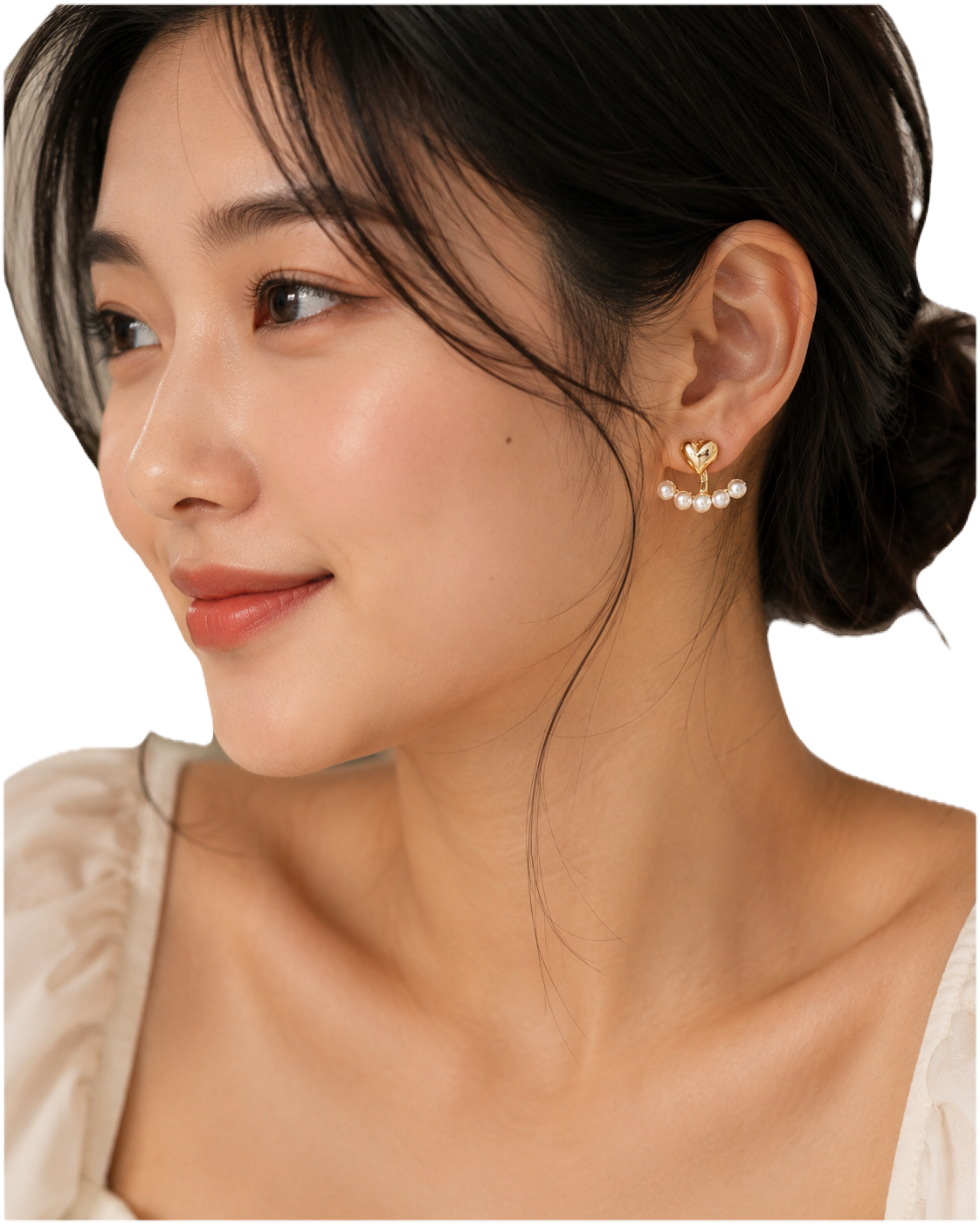 A close-up of a woman wearing a delicate gold heart-shaped dangle earring adorned with small white pearls, shown against a clean white background.
