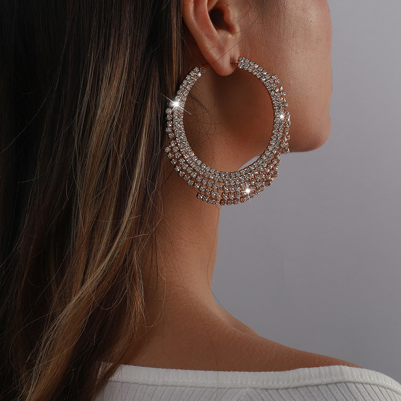 Close-up of a person wearing a sparkling hoop earring against a neutral background