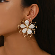 A close-up of a model's ear wearing a large gold flower-shaped earring with white petal-like stones.