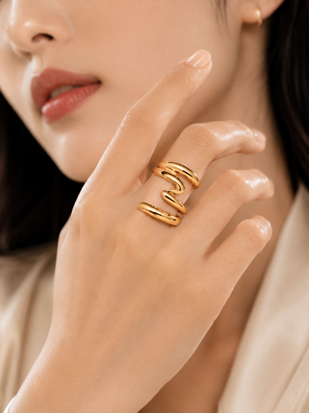 A close-up of a woman's hand wearing a gold wrap ring, with her face partially visible in a softly lit portrait.