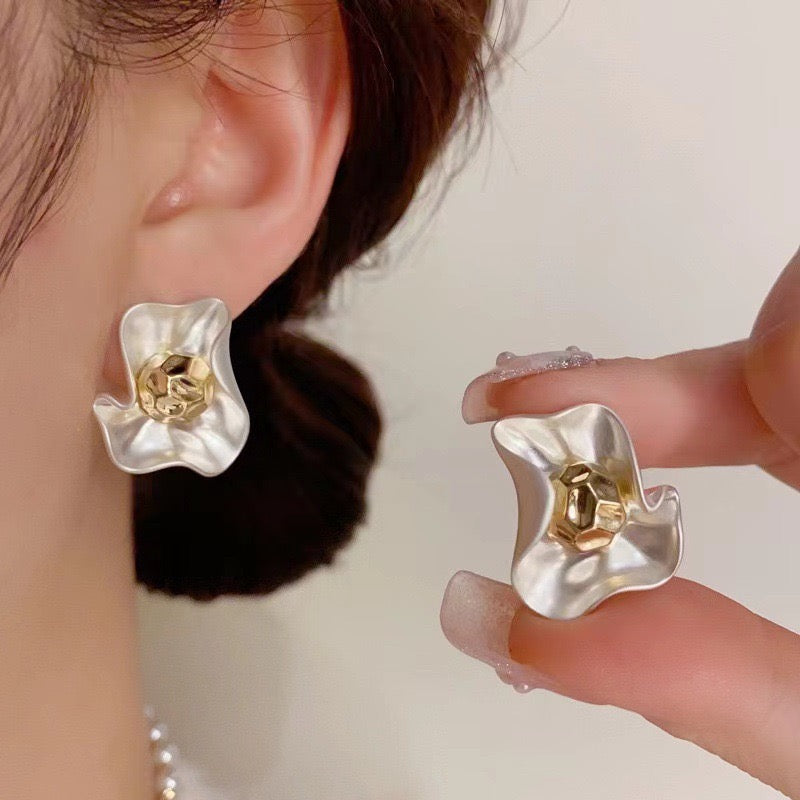 Floral earrings with gold center held by a hand against a neutral background