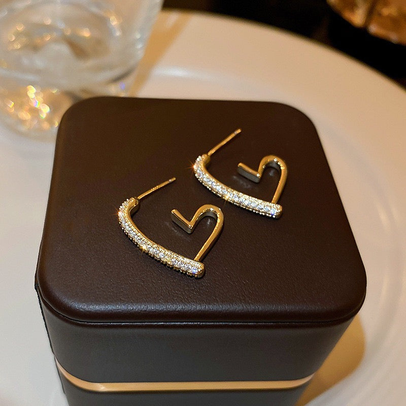 Gold heart-shaped earrings on a brown jewelry box