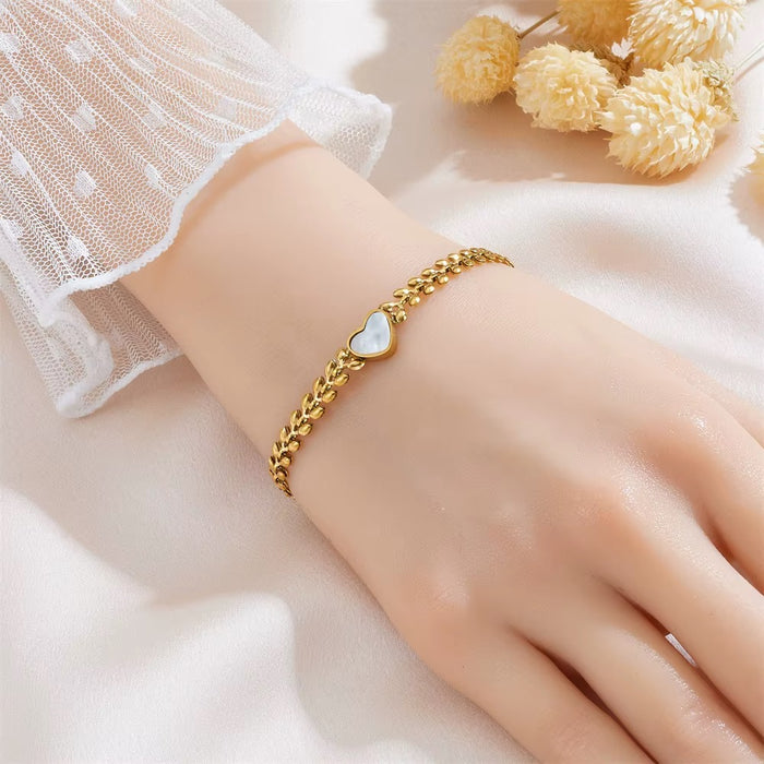 Gold bracelet with a heart charm on a wrist against a soft background
