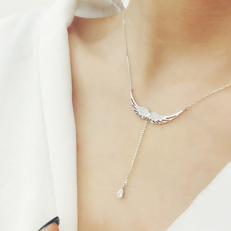 Silver angel wing necklace with a teardrop pendant on a model wearing a white blouse.
