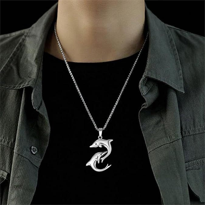 A silver-toned stainless steel pendant necklace featuring two dolphins, worn by a model over a black t-shirt and dark gray button-up shirt.