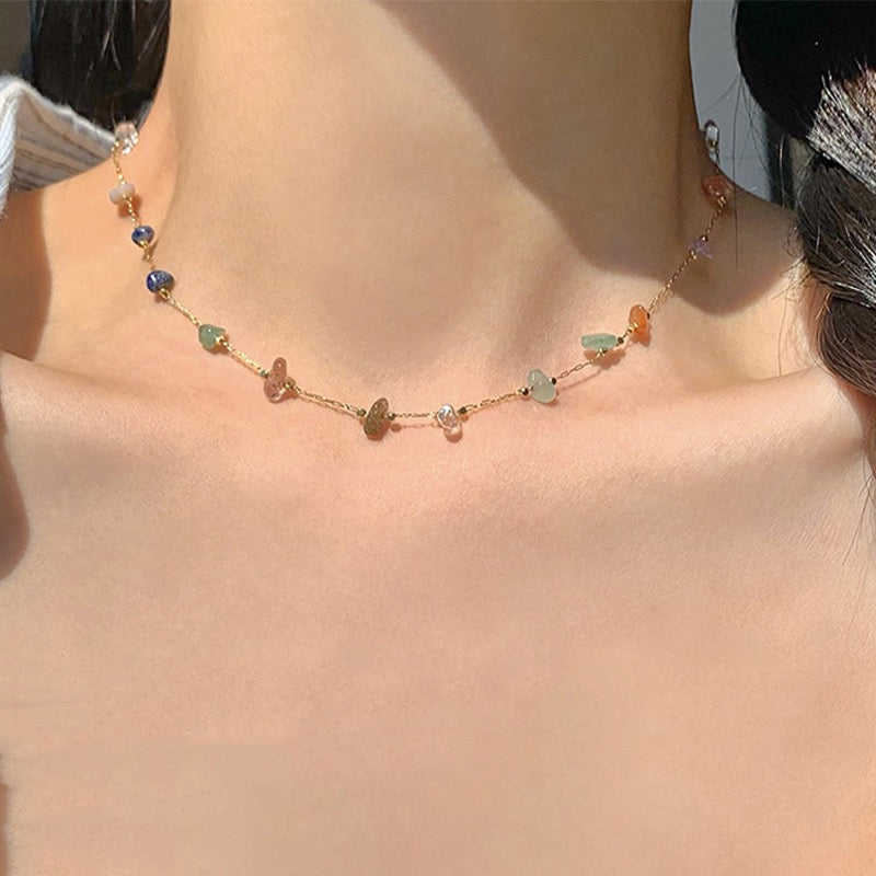 A delicate gold chain necklace with small, multi-colored gemstone beads, worn on a model's neck.
