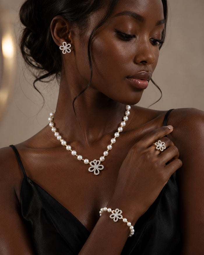 A woman wearing a matching pearl jewelry set with silver-tone flower-shaped connectors, including a necklace, ring, and bracelet, paired with a silver flower earring.