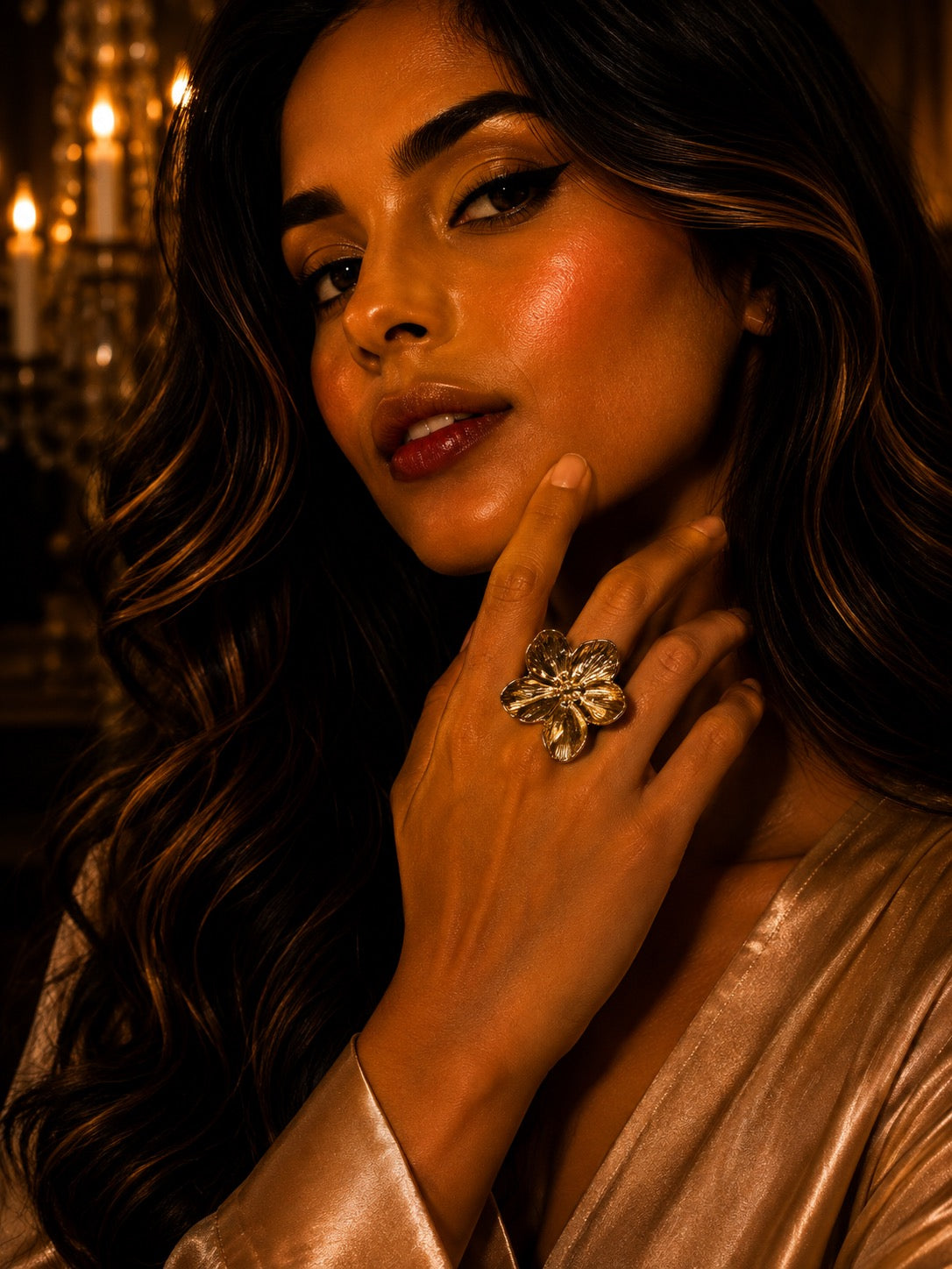 A close-up lifestyle shot of a woman with long wavy brown hair wearing a large, detailed silver ring on her finger, set against a warm, candle-lit background.