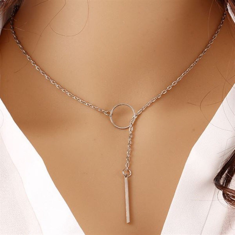 A silver Y-necklace with a delicate chain, a circular ring at the center, and a hanging bar pendant, shown worn on a model's neck.
