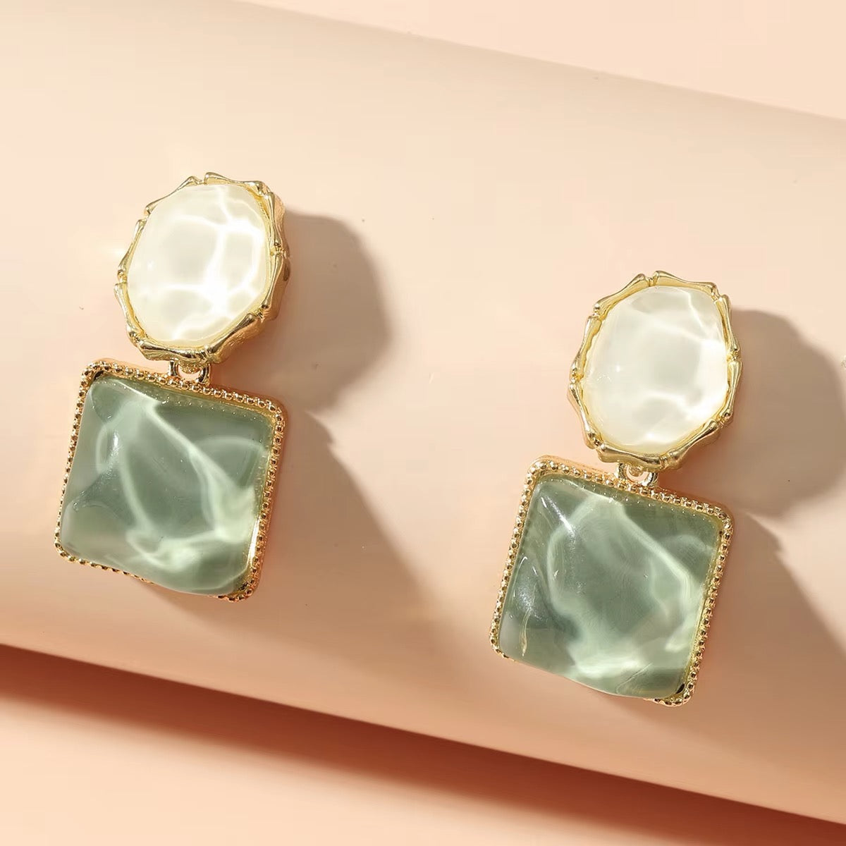 Pair of earrings with green square stones and gold accents on a beige background