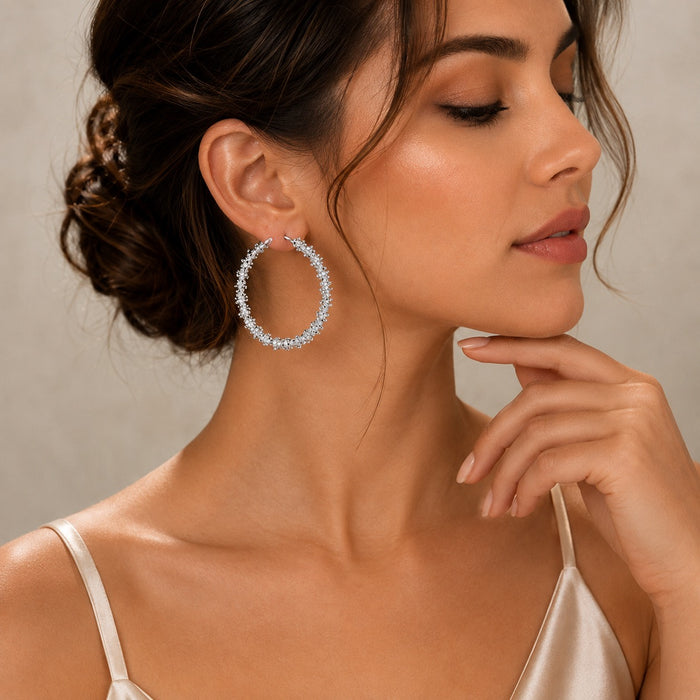 A woman in profile wearing a large silver hoop earring encrusted with clear stones, set against a soft beige background.
