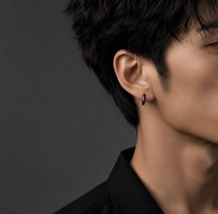 A close-up side profile of a man wearing a small black hoop earring in his ear, set against a dark gray background.
