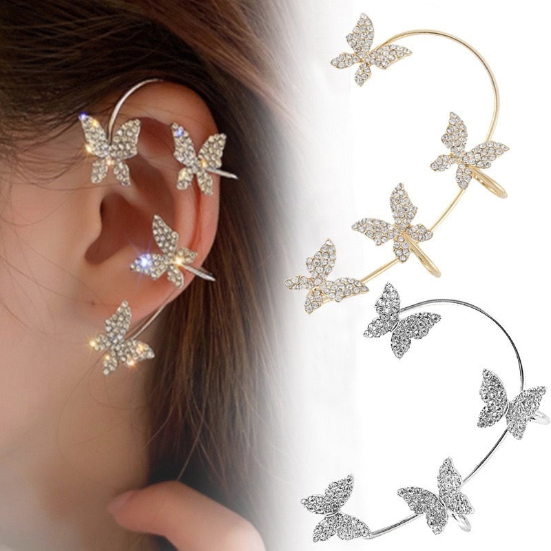 Butterfly-shaped ear cuff earrings shown worn on a person's ear alongside two additional views of the same design in gold and silver tones with rhinestone detailing.