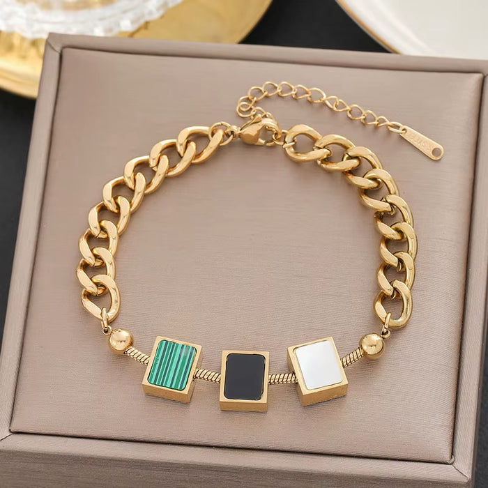 Gold chain bracelet with square charms on a beige box